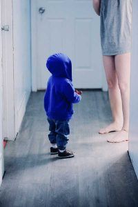 Talking to your young children will help them learn to manage their emotions early on. In the image we see a child standing in the hallway at home with one of his parents. 